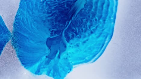 Blue-ink-spreading-in-water-with-a-frost-like-texture-and-sparkling-particles,-simulating-ice-formation