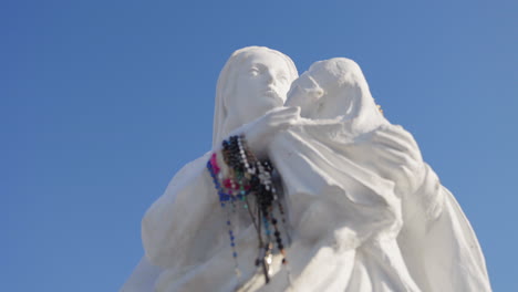 Wunderschöne-Weiße-Statue-Der-Jungfrau-Maria,-Die-Jesus-In-Ihren-Armen-Trägt,-Mit-Einem-Wunderschönen-Blauen-Himmel-Im-Hintergrund-Auf-Dem-Hügel-Der-Kreuze