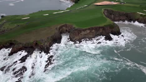 Waves-crashing-against-the-cliffs-along-Pebble-Beach-golf-course---pullback-aerial-reveal