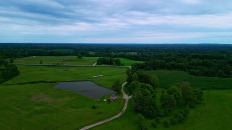 Aerial-view-of-a-landscape-with-green-meadows,-a-lake-and-highway-in-the-background