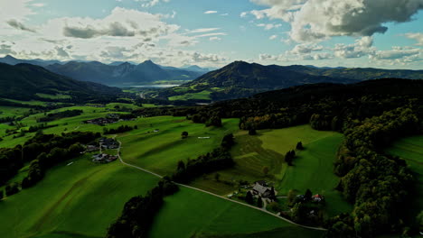 Lush-green-valley-with-scattered-houses,-flanked-by-mountains-under-a-partly-cloudy-sky,-aerial-view