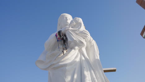 Wunderschöne-Weiße-Statue-Der-Jungfrau-Maria,-Die-Jesus-In-Ihren-Armen-Trägt,-Mit-Einem-Wunderschönen-Blauen-Himmel-Im-Hintergrund-Auf-Dem-Hügel-Der-Kreuze