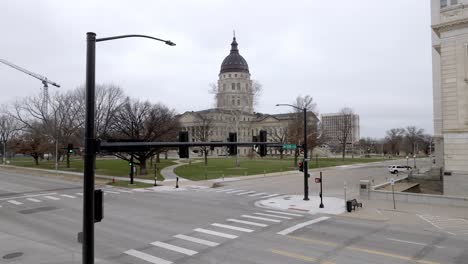 Kansas-state-capitol-building-with-flags-waving-in-wind-in-Topeka,-Kansas-with-drone-video-pulling-back