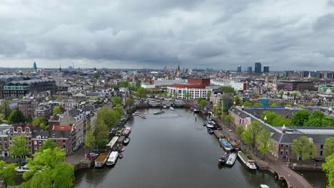 The-drone-is-flying-forward-over-the-Amster-canal-looking-towards-the-city-centre-and-the-national-opera-and-ballet-on-a-cloudy-day-in-Amsterdam-The-Netherlands-Aerial-Footage-4K
