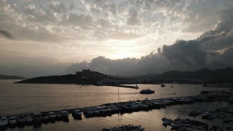 Die-Drohne-Fliegt-über-Einen-Hafen-Mit-Dunklen-Wolken-Im-Hintergrund-In-Ibiza,-Spanien,-Luftaufnahmen-4k