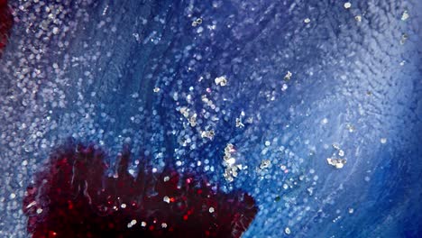Tinta-Azul-Y-Roja-Que-Se-Dispersa-En-Agua-Con-Partículas-Brillantes,-Creando-Un-Fondo-Celestial-Abstracto