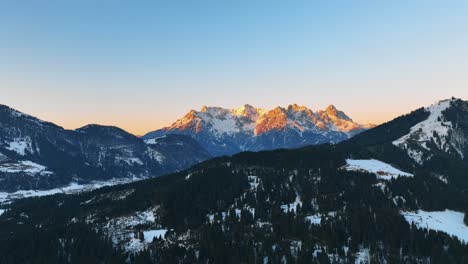 The-drone-is-flying-over-a-mountain-with-trees-towards-the-big-mountain-lit-by-the-golden-sun-during-sunset-in-Austria-Aerial-Footage-4K