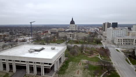 Kansas-state-capitol-building-with-flags-waving-in-wind-in-Topeka,-Kansas-with-drone-video-circling-wide-shot