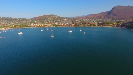Aerial-view-of-many-sailboats-anchored-in-a-calm-water-bay-off-the-coast-of-a-Mexican-city-tucked-into-the-mountains-near-Zihuatanejo