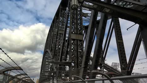 Handheld-Shot-Walking-Across-Sydney-Harbour-Bridge-Footpath-Looking-Up-At-Steelwork