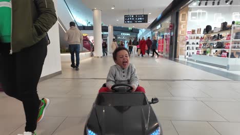 Glückliches-3-jähriges-Schwarzes-Kind,-Das-In-Einem-Einkaufszentrum-Ein-Elektrisches-Schwarzes-Spielzeugauto-Fährt