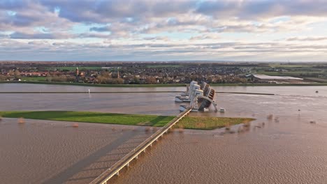 Aerial-orbit-drone-shot-to-the-right-at-the-weir-of-Driel-during-high-water-levels-with-the-doors-open-and-with-the-town-of-Driel-in-the-background