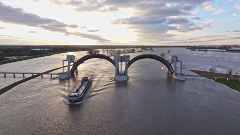 Aerial-orbit-drone-shot-to-the-right-at-the-weir-of-Driel-during-high-water-levels-with-the-doors-open-and-a-ship-passing-thru-the-weir