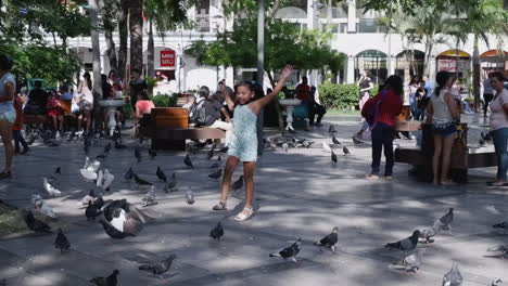Young-girl-chases-pigeons-in-busy-city-plaza-in-Santa-Cruz,-Bolivia