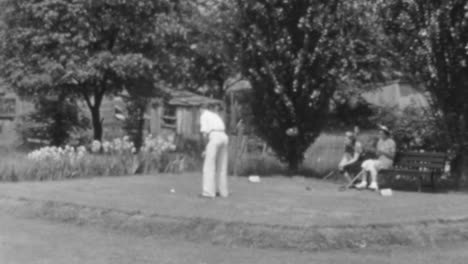 Un-Hombre-Juega-Golf-Con-Una-Mujer-Sentada-Al-Fondo-Mirando-En-Nueva-York-En-1930