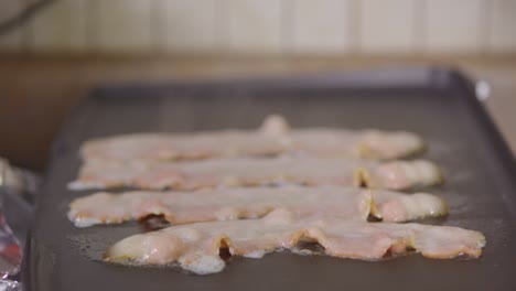 Close-up-of-raw-bacon-cooking-on-a-griddle