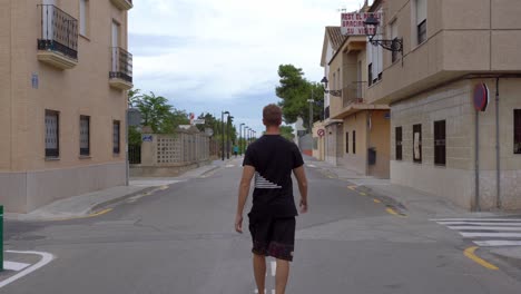Back-view-of-young-man-walking-in-middle-of-street,-opening-his-arms-happily,-Valencia