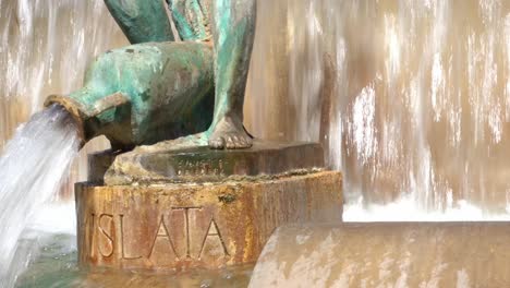 Dolly-left-shot-of-bronze-statue-feet-with-jug-in-fountain