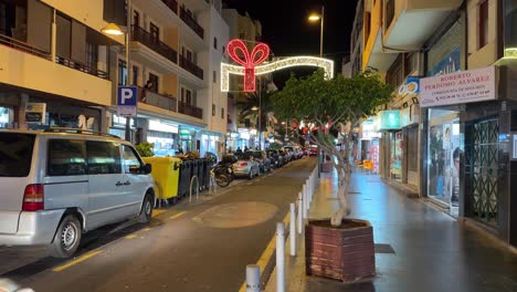Los-Cristianos-street-in-Tenerife-at-night,-cars-passing-on-main-road,-Spain