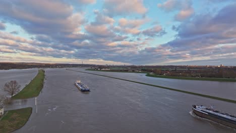 Folgende-Drohnenaufnahme,-Während-Frachtschiffe-Bei-Hohem-Wasserstand-Auf-Dem-Fluss-Rijn-Aneinander-Vorbeifahren