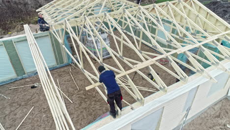 Two-carpenters-install-the-ready-made-wooden-roof-trusses-on-a-prefabricated-house