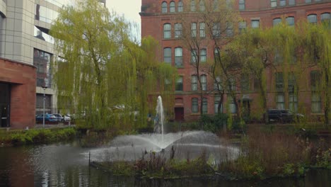 Presence-of-a-fountain-in-a-pond-in-City-Centre-of-Manchester-during-a-cloudy-winter-morning-in-England