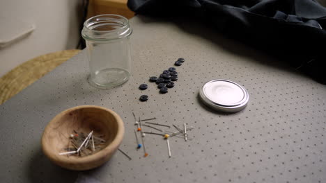 Pot-of-pins-with-needle-and-buttons-in-seamstress's-fashion-studio