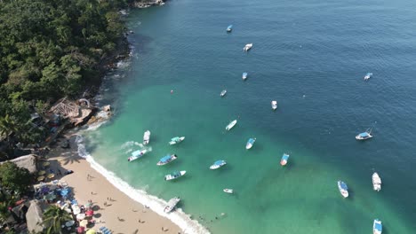 Boats-anchored-in-clear-green-waters-off-coast-of-Playa-Mismaloya-Mexico,-aerial-bird's-eye-view