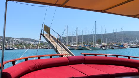 Wooden-stern-on-a-big-sailing-boat-in-Bodrum-Turkey-with-yachts,-fun-summer-vacation,-the-rear-back-of-a-moving-boat,-luxury-holiday-destination,-sunny-sea-day-with-blue-sky,-4K-shot