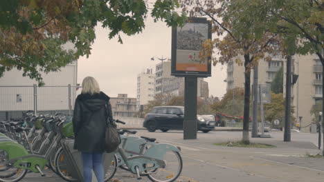 Mujer-Rubia-Pasando-Por-Bicicletas-De-La-Ciudad-Estacionadas-En-Una-Calle