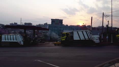 Garbage-trucks-at-a-petrol-station-in-downtown-Yaounde,-sunset-in-Cameroon,-Africa