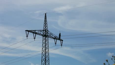 Electricity-pylon-with-worker-against-a-cloudy-blue-sky-with-visible-cables-and-surrounding-foliage