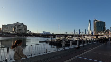 Menschen,-Die-Am-Ufer-Von-Darling-Harbour-In-Sydney-Herumlaufen,-Während-Fahnen-Im-Wind-Wehen