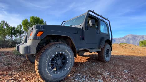 Black-Jeep-4x4-car-on-a-sunny-day-on-La-Quinta-mountain-top-with-green-trees-and-blue-sky,-fun-ATV-adventures-in-Marbella-Malaga-Spain,-4K-shot
