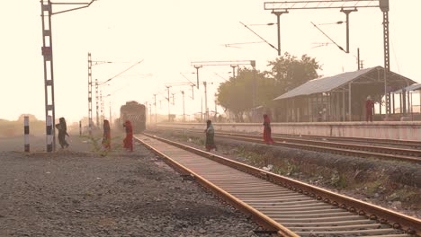 Gruppe-Traditioneller-Indischer-Frauen,-Die-Während-Des-Sonnenuntergangs-Bahngleise-An-Einem-Bahnhof-überqueren
