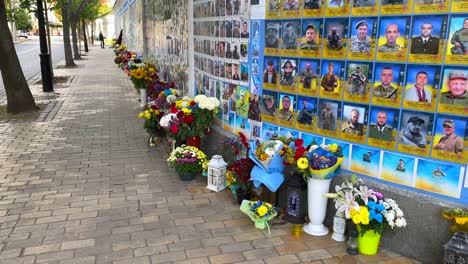Long-memorial-wall-of-fallen-soldiers-in-Kyiv-Ukraine,-wall-of-honor-for-the-soldiers-who-died-during-the-Russia-Ukraine-war-battle,-honoring-and-remembering-flowers,-4K-shot