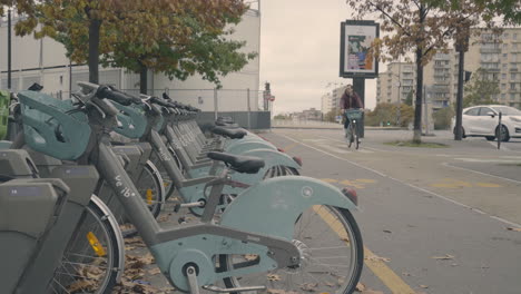 Un-Hombre-Anda-En-Bicicleta,-La-Estaciona-En-Un-Estacionamiento-Urbano-De-Bicicletas-En-La-Calle-Y-Se-Aleja
