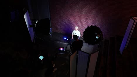 Guy-sit-in-dark-podcast-studio-environment-near-illuminated-brick-wall