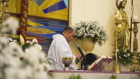 Adult-priest-with-alopecia-cleaning-container-during-the-ceremony-of-the-sacrament-of-communion-at-the-altar-of-catholic-church