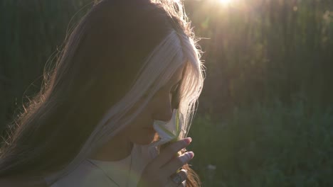 Beautiful-young-woman-smelling-flower-in-nature-illuminated-by-sun-at-sunset