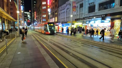 Night-shot-of-tram-arriving-at-light-rail-stop-outside-the-Queen-Victoria-Building,-Sydney