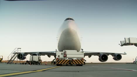 Front-view-of-a-large-cargo-airplane,-ground-crew-working-during-golden-hour