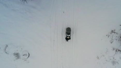 Aerial-top-down-view-of-female-push-baby-carriage-on-snowy-road-under-trees
