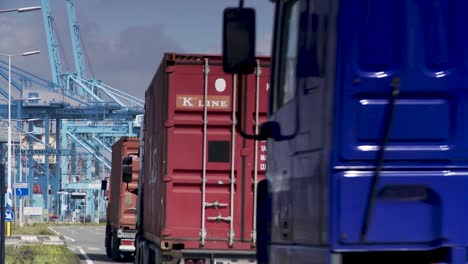 Trucks-in-motion-towards-port-with-cargo-containers-and-cranes-in-background,-clear-day