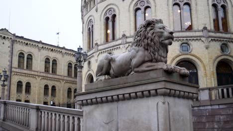 The-parliament-building-in-central-Oslo,-Norway-and-statue-of-a-lion-on-a-winter-day