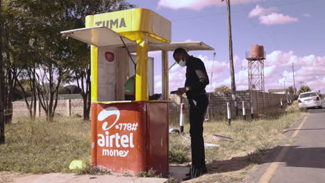 A-customer-approaches-an-agent-to-make-a-financial-transaction-at-a-mobile-money-kiosk-on-the-streets-of-Lusaka,-Zambia