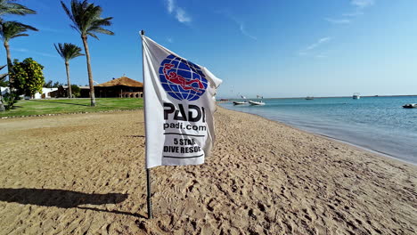 PADI-five-star-dive-resort-flag-waving-in-the-wind-at-a-beach-in-sunny-Dahab,-Egypt