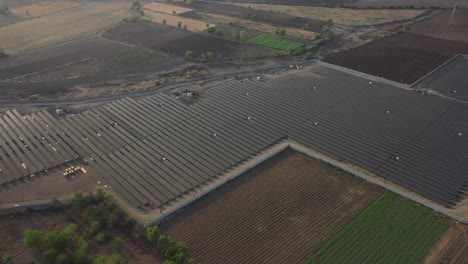 Aerial-drone-view-showing-a-large-solar-power-plant-in-a-large-field-surrounded-by-bushes-and-a-road