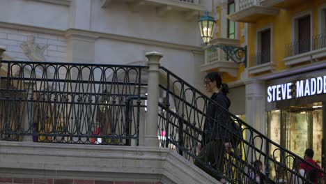 Woman-walks-up-stairs-and-across-bridge-at-the-Grand-Canal,-Venetian-Resort-shopping-mall-interior