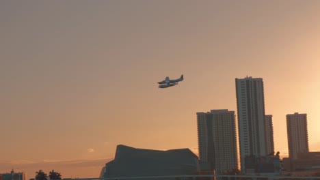 Float-plane-flying-low-over-a-bridge-in-Miami-during-sunset,-panning-left